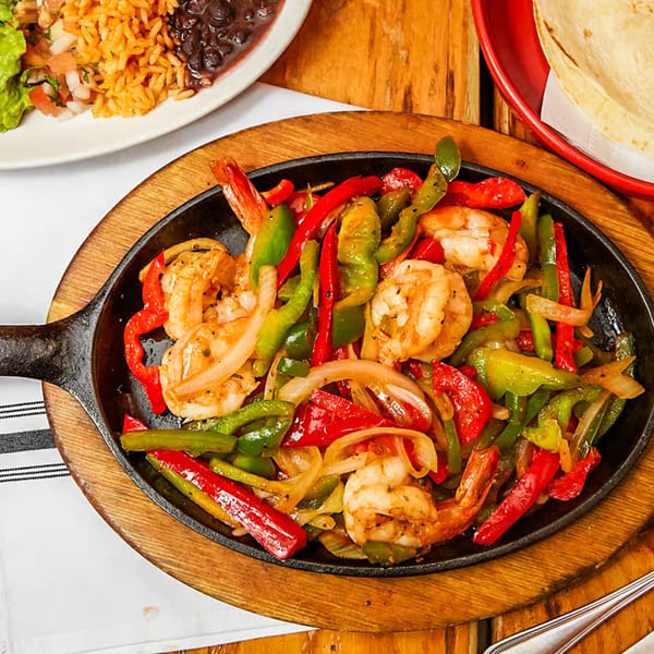 Sizzling shrimp fajitas with red and green bell peppers and onions in a cast iron skillet.