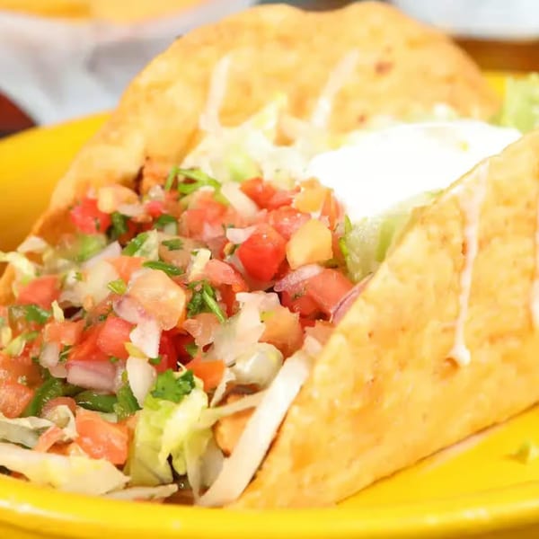 Crispy Patron Mexican Grill taco filled with pico de gallo, lettuce, and sour cream on a yellow plate.
