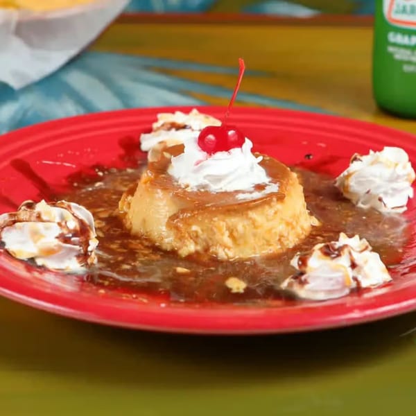 Flan dessert with caramel sauce, whipped cream, and a cherry on a red plate at Patron Mexican Grill.
