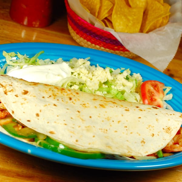 Shrimp fajita on a blue plate with lettuce, cheese, tomato, sour cream, and tortilla chips.
