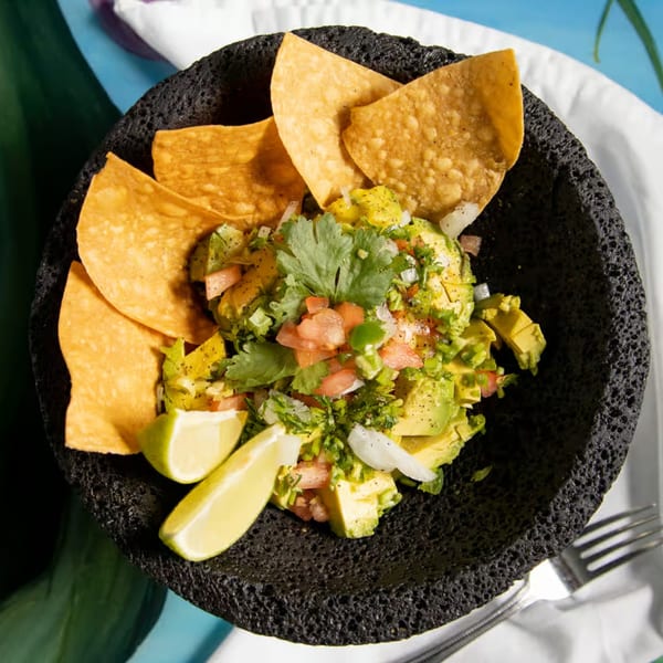 Fresh guacamole with tortilla chips, lime wedges, cilantro, and diced tomatoes in a dark bowl.