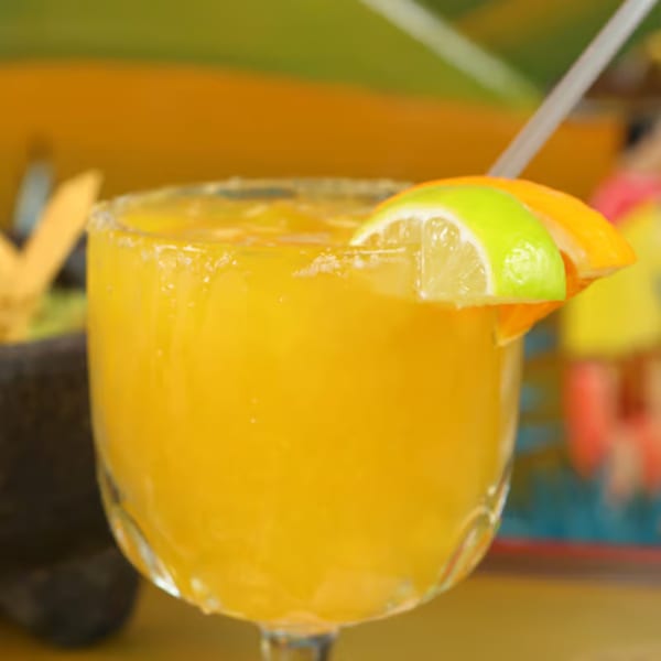 Close-up of a vibrant orange margarita with lime and orange slices, and a straw.